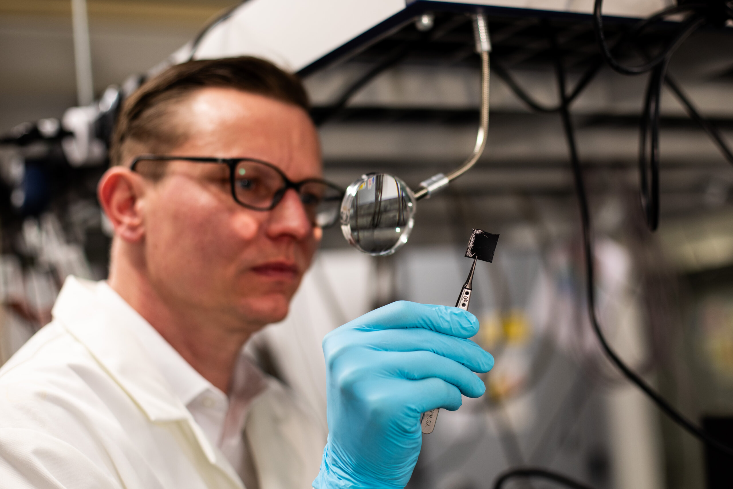 A man in a lab coat studies a microchip through a magnifying glass in a laboratory