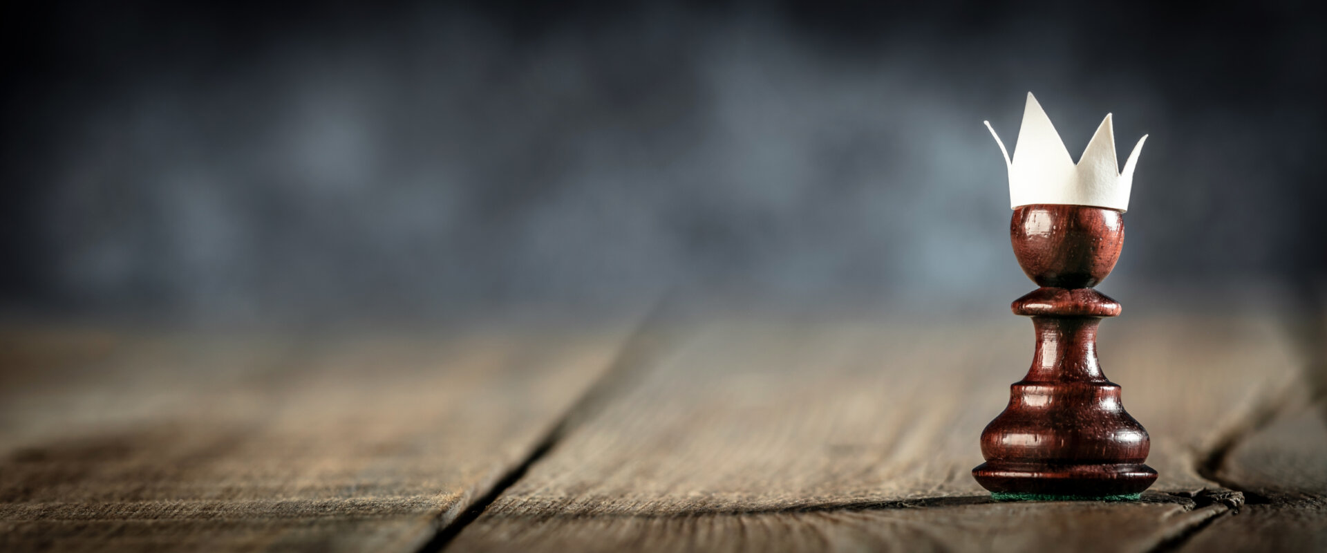 a pawn chess piece sits on a wooden surface with a paper crown - signifying start ups/beginning as an entrepreneur