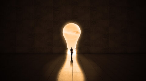 Concept of entrepreneurship, a person walking through a lightbulb shaped door in to the light.